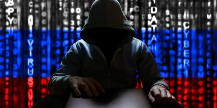 Unknown Russian hacker opens the lid of a laptop, sitting on the background of the Russian flag from a binary code.