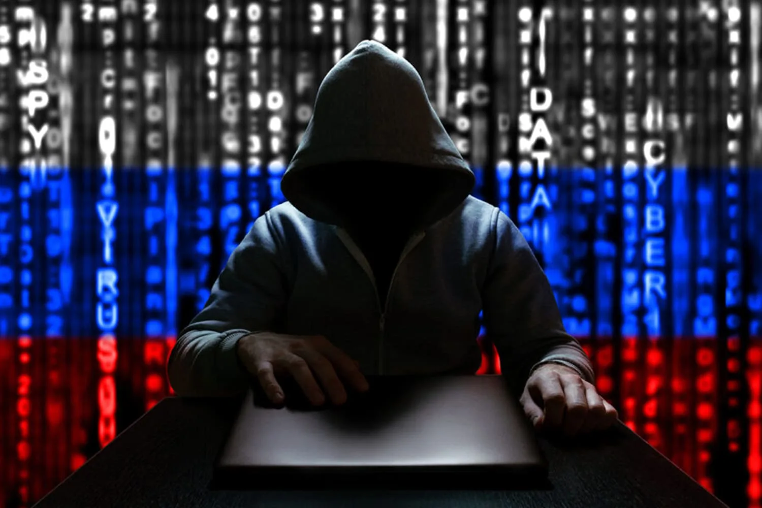 Unknown Russian hacker opens the lid of a laptop, sitting on the background of the Russian flag from a binary code.