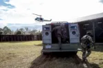 Miembros del Equipo de Respuesta a Emergencias del Centro Espacial Kennedy de la NASA salen de un vehículo táctico durante un ejercicio de respuesta a un tirador activo en las instalaciones de entrenamiento de Servicios de Protección del centro. Un helicóptero sobrevuela la zona. Equipo de Respuesta a Emergencias de la NASA/KSC