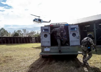 Miembros del Equipo de Respuesta a Emergencias del Centro Espacial Kennedy de la NASA salen de un vehículo táctico durante un ejercicio de respuesta a un tirador activo en las instalaciones de entrenamiento de Servicios de Protección del centro. Un helicóptero sobrevuela la zona. Equipo de Respuesta a Emergencias de la NASA/KSC