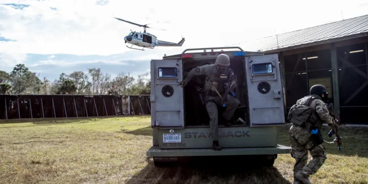 Miembros del Equipo de Respuesta a Emergencias del Centro Espacial Kennedy de la NASA salen de un vehículo táctico durante un ejercicio de respuesta a un tirador activo en las instalaciones de entrenamiento de Servicios de Protección del centro. Un helicóptero sobrevuela la zona. Equipo de Respuesta a Emergencias de la NASA/KSC