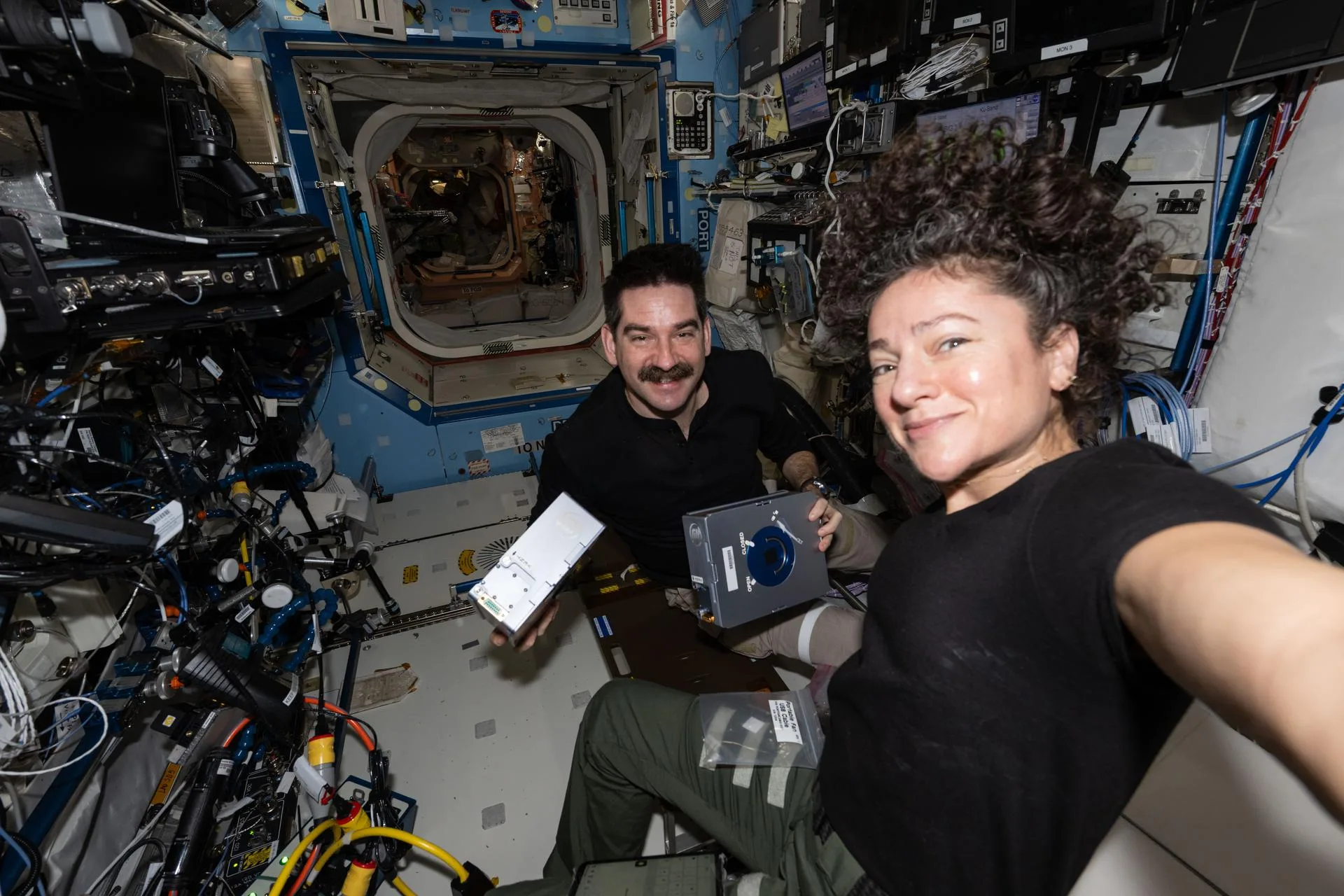 Los astronautas de la NASA Jack Hathaway y Jessica Meir posan juntos mientras Hathaway muestra un par de casetes de investigación del Procesador de Muestras de Experimento Espacial Avanzado-4 que se utilizan para estudiar cómo la ingravidez afecta el crecimiento de cristales de fármacos, lo que posiblemente conduzca a nuevas fórmulas farmacéuticas. Crédito: NASA.