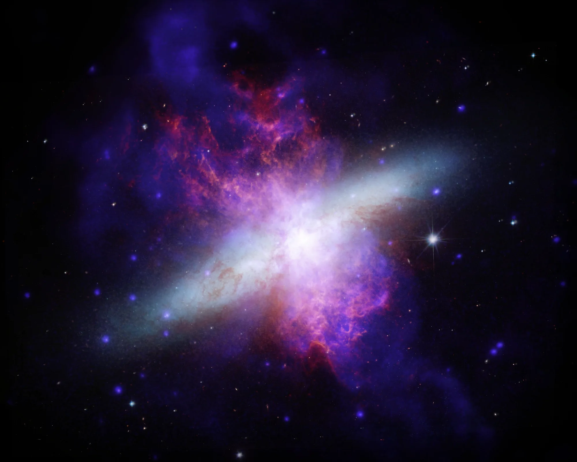 Imagen infrarroja de M82, una galaxia irregular que atraviesa un intenso proceso de formación estelar. Se observan densas columnas de gas turbulento de color fucsia emergen por encima y por debajo de un disco galáctico azul pálido. Crédito: NASA/ Telescopio Espacial James Webb (JWST).