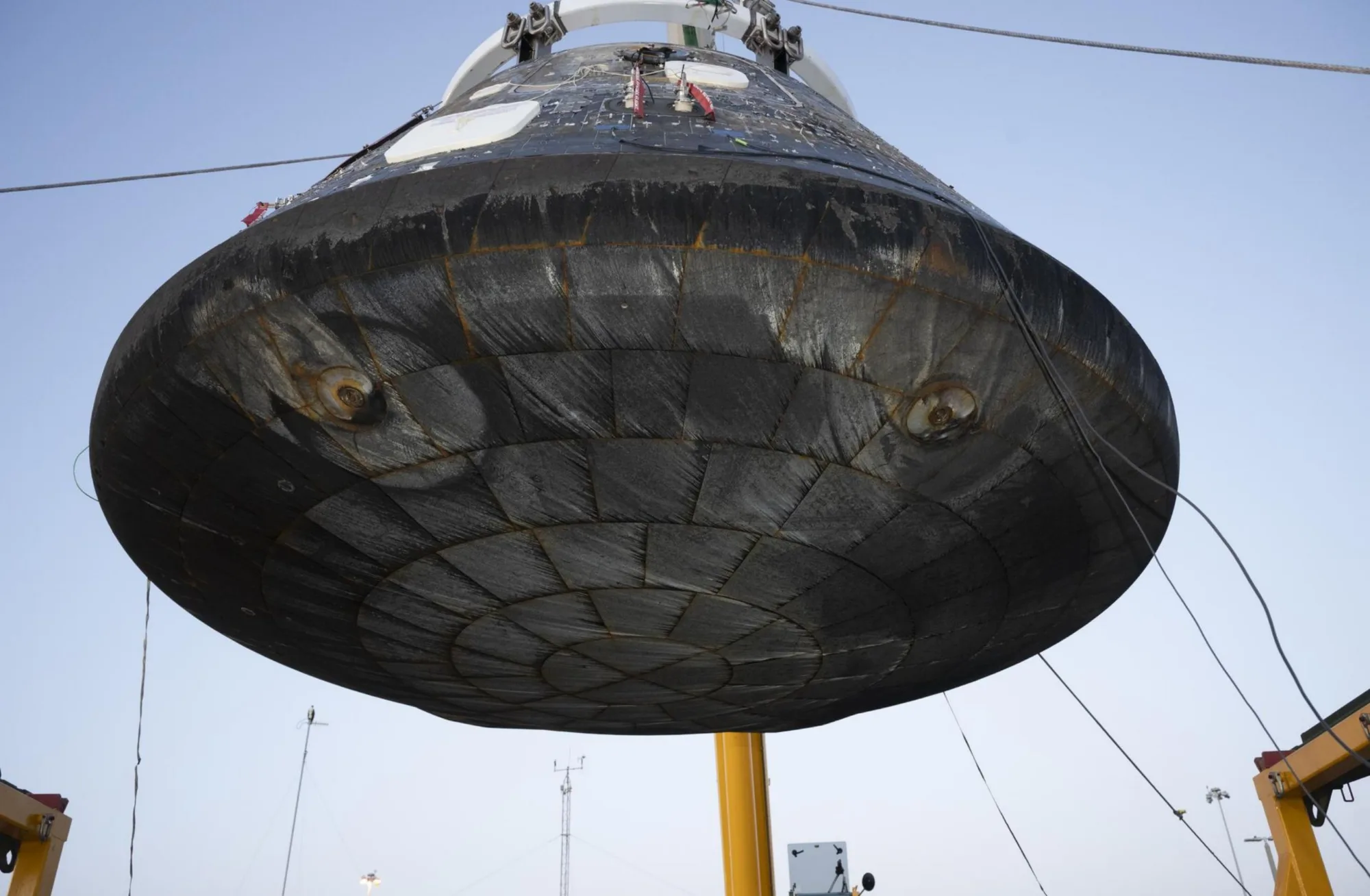 El módulo de tripulación Artemis II Orion luego de la recuperación, siendo elevado para su inspección tras ser descargado del buque de recuperación USS John P. Murtha. Las áreas hundidas, o círculos concéntricos más pequeños están asociadas con los pernos de separación que conectan el módulo de tripulación con el módulo de servicio. Los patrones circulares más grandes se forman debido al material de la almohadilla de compresión, lo que crea perturbaciones en el flujo causadas por el flujo de aire aerodinámico y térmico extremo durante la reentrada. Crédito: NASA/ Kevin Davis.